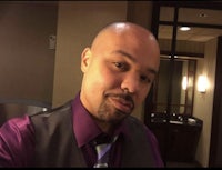 a bald man in a purple vest and tie taking a selfie